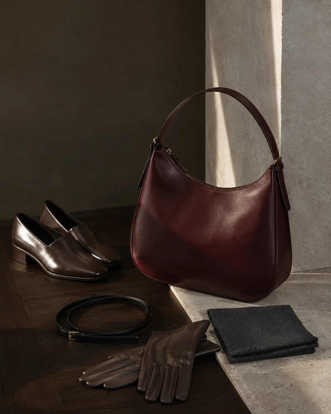 Schwarze Ledertasche, Gürtel, flacher Schuh und Handschuhe auf dunklem Stein